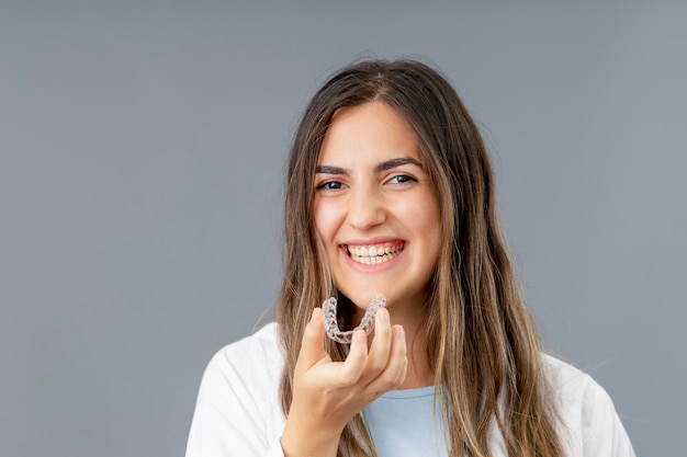 Красивая улыбающаяся турецкая женщина держит браслет invisalign в студии на сером фоне с копировальным пространством