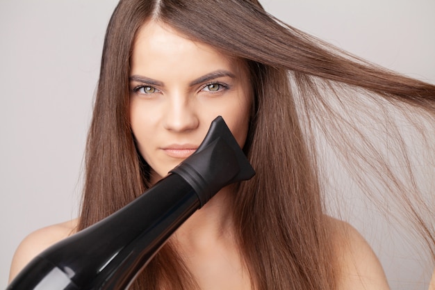 Beautiful smiling woman drying her long hair with dryer