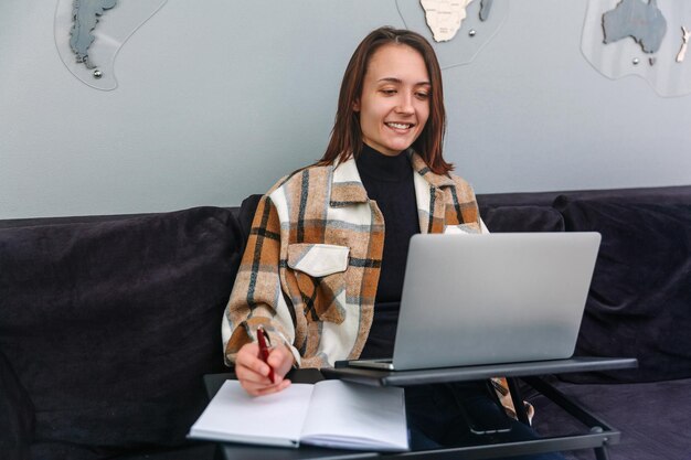 Photo beautiful smiling woman looking at laptop and writing note in notepad