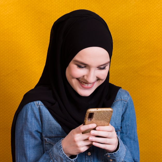 Beautiful smiling woman reading messages on smartphone over yellow backdrop