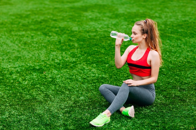 Beautiful Smiling Woman Relaxing on the Grass in the Park During Training. Sport and Fitness Concept