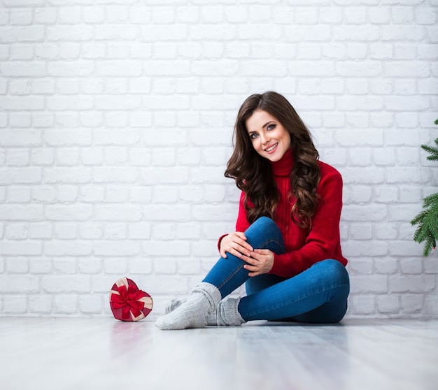 Bella donna sorridente seduta sul pavimento accanto a un regalo