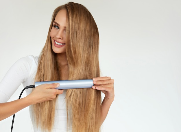 Foto bella donna sorridente che raddrizza i capelli biondi lunghi sani