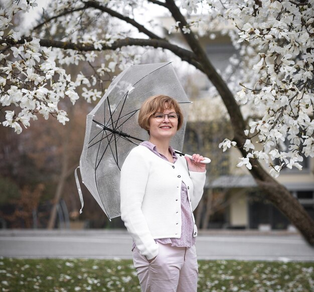 Beautiful smiling woman umbrella against background white flowering magnolia