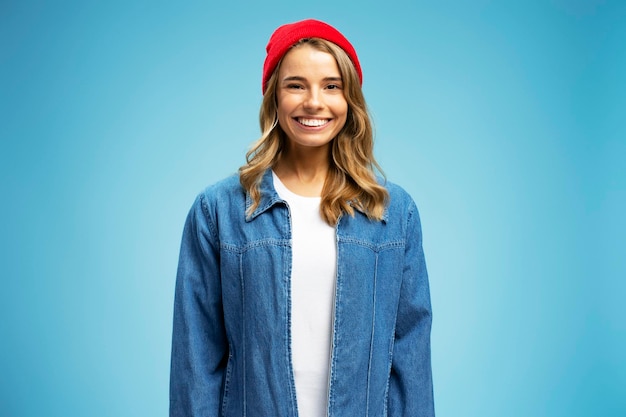 Beautiful smiling woman wearing red hipster hat and stylish jeans jacket isolated on blue background