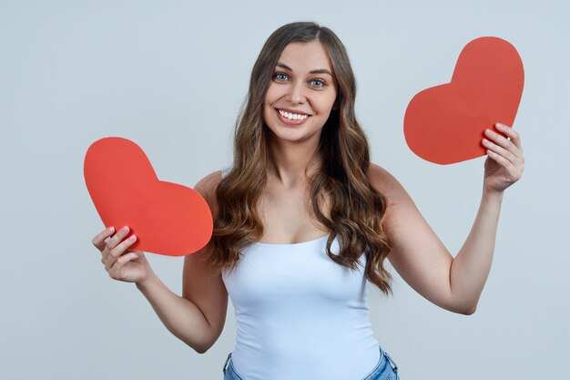 A beautiful smiling woman in a white T-shirt, holding two red hearts in her hands