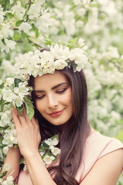 春の花の背景に健康的な茶色の髪型と花のメイクで美しい笑顔の女性