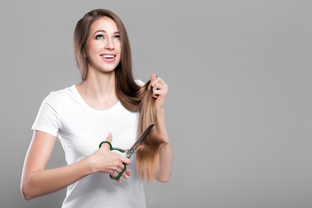 Beautiful smiling woman with straight long hair holds scissors for hairstyle