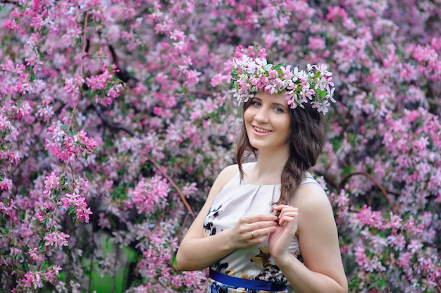 Beautiful smiling woman with a wreath in the blossoming spring garden