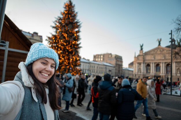 背景に市の正方形のクリスマス ツリーで selfie 写真を撮る美しい笑顔の女性