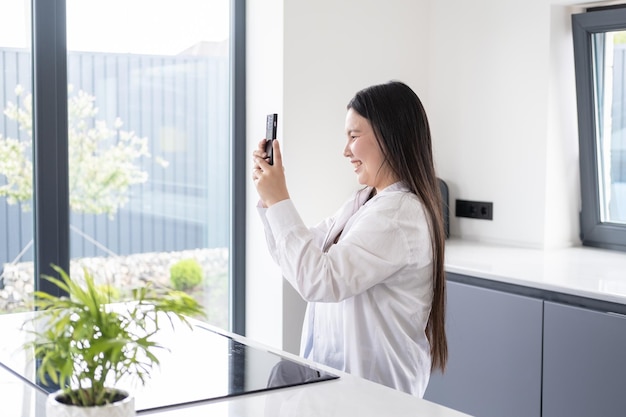 Bella giovane donna asiatica sorridente con i capelli lunghi scuri che utilizza il telefono all'interno moderno