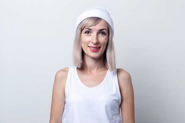 Beautiful smiling young blonde woman in a white hat on a light background.