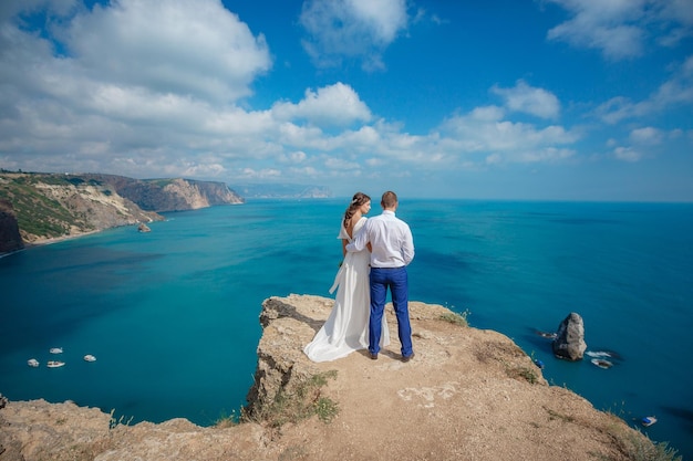 Beautiful smiling young bride and groom walking on the beach kissing and having fun wedding ceremony near the rocks and sea Wedding ceremony on coast of Cyprus