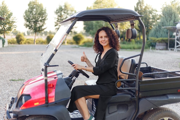 Beautiful smiling young brunette curly woman in black dress showing ok sign posing in vehicle outside