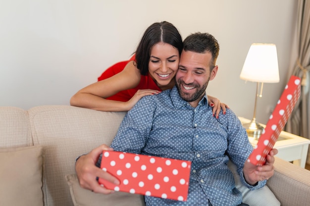 Beautiful smiling young couple celebrating love for birthday or anniversary Attractive woman surprising him with a present