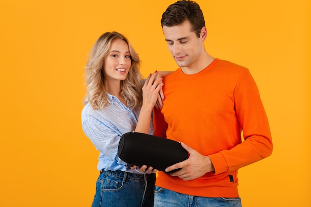 Beautiful smiling young couple holding wireless speaker listening to music colorful style happy mood isolated on yellow wall