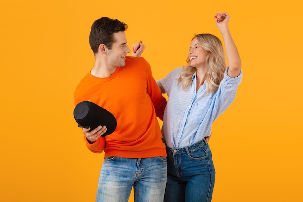 Beautiful smiling young couple holding wireless speaker listening to music dancing emotional