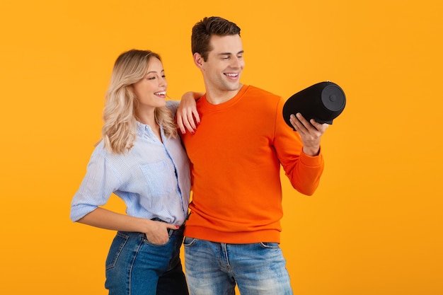 Beautiful smiling young couple holding wireless speaker listening to music on orange