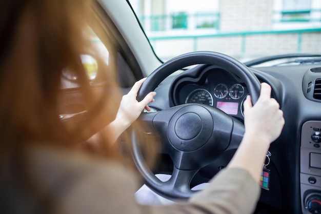 Beautiful smiling young redhead woman behind steering wheel driving car