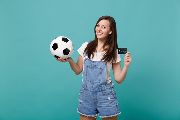 Beautiful smiling young woman football fan support favorite team with soccer ball, credit bank card isolated on blue turquoise wall background. People emotions, sport family leisure lifestyle concept.