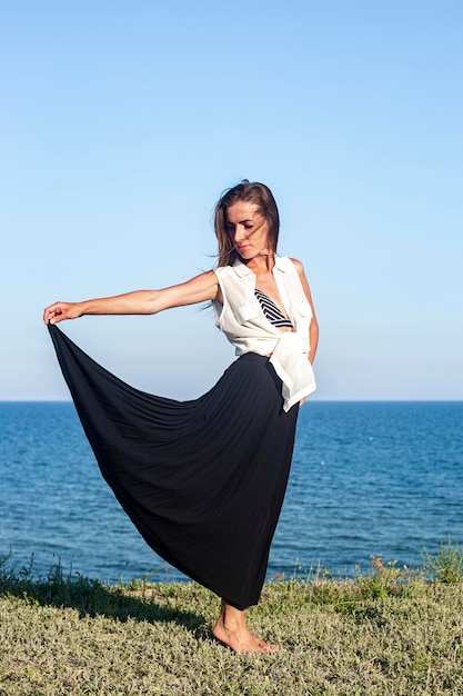 Beautiful smiling young woman holding a skirt while standing on a cliff