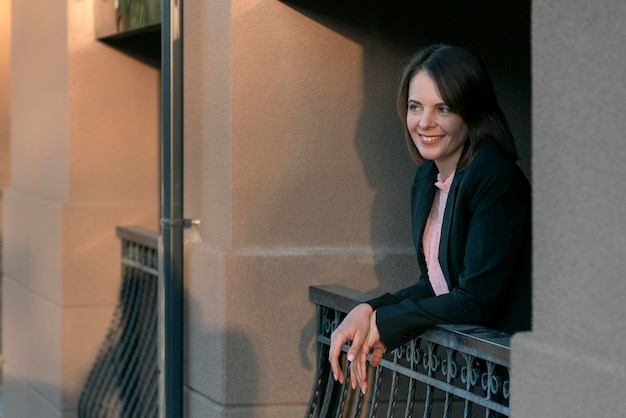 Beautiful smiling young woman is resting on the balcony Woman in business attire on a break