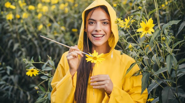 Beautiful smiling young woman paint yellow flowers pretty cheerful smiling girl wearing yellow hoodi