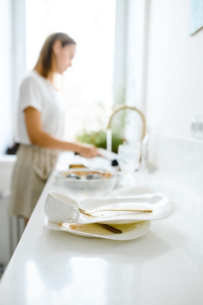 Foto bella giovane donna sorridente che lava i piatti in cucina bianca moderna.