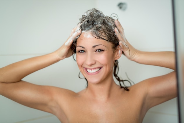 Beautiful smiling young woman washing her long hair with shampoo.