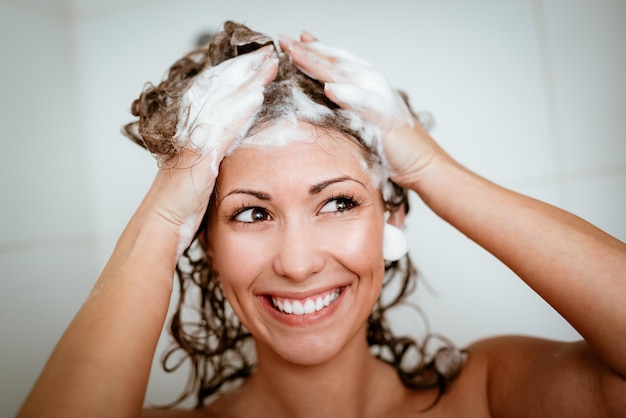 Photo beautiful smiling young woman washing her long hair with shampoo.