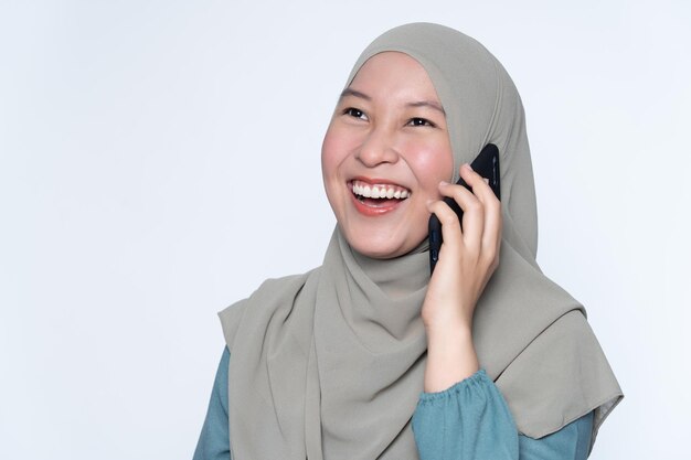 Beautiful smiling young woman wearing hijab talking on smart phone while standing against white background