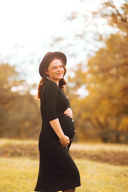 красивая улыбающаяся молодая женщина, которая беременна в парке