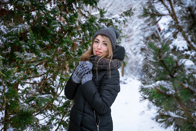 暖かいジャケットを着た冬の屋外の美しい笑顔の若い女性は、雪に覆われた中で天気を楽しんでいます...