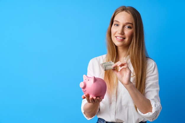 Beautiful smiling young woman with piggy bank on blue background