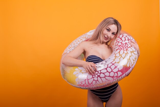 Beautiful smilling young woman with long blonde hair with stylish swimming suit posing over yellow background. Sexy young woman in blue swimming suit.