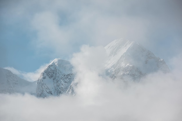 Beautiful snow castle in low clouds Lovely scenery with high snowy mountains in thick clouds Big air castles float in gantly cloudy sky Scenic view to large snow mountain in clearance of dense fog