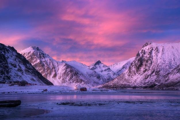 Beautiful snow covered mountains and blue sky with pink clouds and frozen sea coast at sunset Winter landscape with sea house snowy rocks fjord Lofoten islands Norway at dusk Nature background