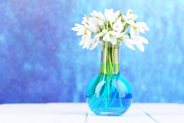 Beautiful snowdrops in vase on wooden table on bright background