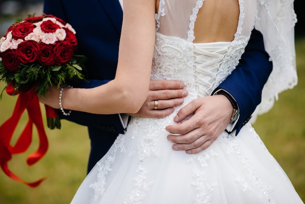 Il primo piano bello e sofisticato del mazzo di nozze tiene la sposa in sue mani vicino allo sposo. bouquet da sposa e anelli.