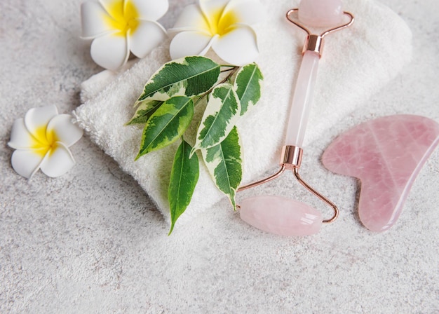 Beautiful spa relax concept towel jade roller and frangipani flowers on grey stone background