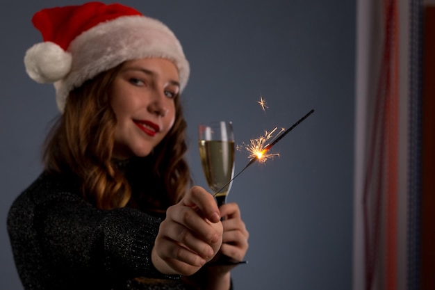 Beautiful sparklers and a glass of champagne in a woman hands on gray background Looks and smiles into the camera isolated on gray background