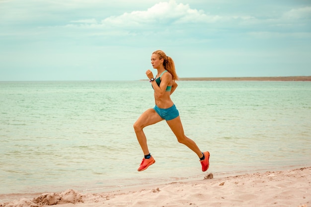 Beautiful sportive woman running along beautiful sandy beach healthy lifestyle enjoying active summer vacation near the sea