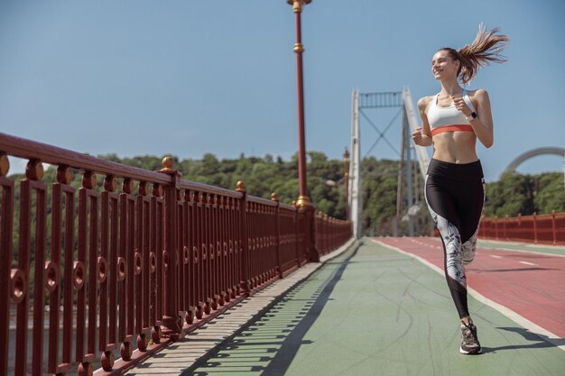 Beautiful sportive woman wearing tracksuit runs along empty footbridge