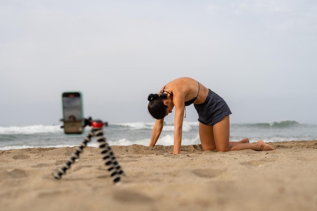Photo beautiful sports girl blogger trains on the sand on takes pictures of herself on a mobi