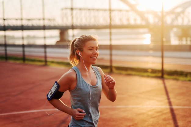 Beautiful sporty fit blond girl listening to the music and running early in the morning outside.