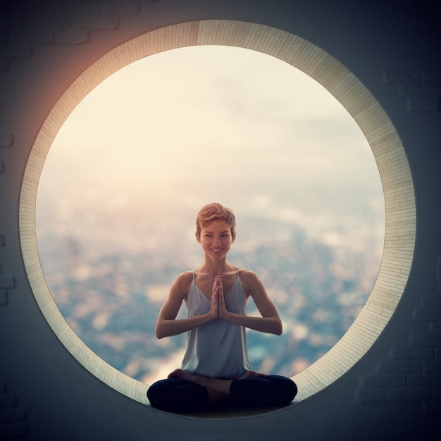 Beautiful sporty fit yogi woman practices yoga asana Padmasana - Lotus pose in a round window