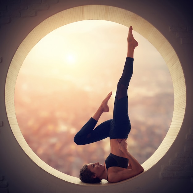 Photo beautiful sporty fit yogi woman practices yoga salamba sarvangasana - shoulderstand pose in a window