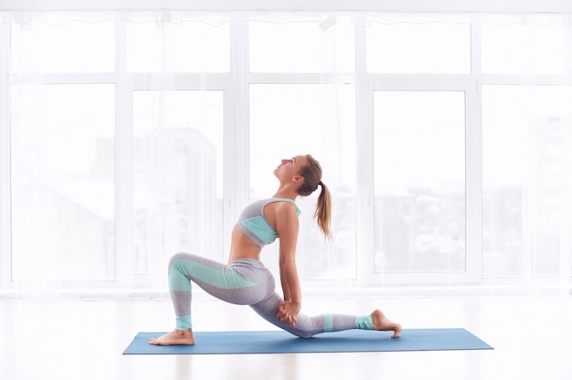 Beautiful sporty fit yogini woman practices yoga asana Ashva Sanchalasana - equestrian pose at the yoga studio