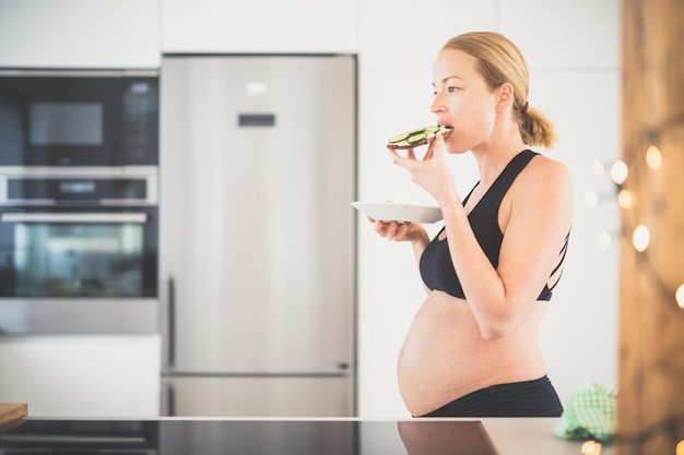 Beautiful sporty fit young pregnant woman having a healthy snack in home kitchen Healty lifestyle concept