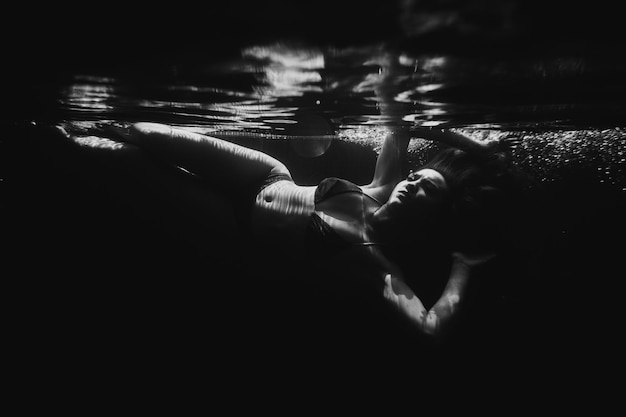 A beautiful sporty girl poses underwater with loose hair against the bright rays of the sun